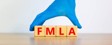 FMLA, family medical leave act symbol. Concept words 'FMLA, family medical leave act' on cubes on a beautiful white background. Doctor hand in blue glove. Copy space. Medical, FMLA concept. clipart