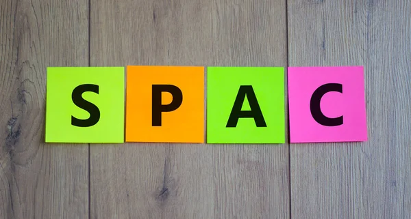 SPAC, special purpose acquisition company symbol. Colored papers with word 'SPAC' on beautiful wooden background, copy space. Business and SPAC, special purpose acquisition company concept.