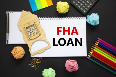 FHA federal konut yönetimi kredi sembolü. Güzel siyah arka planda 'FHA kredisi' yazan beyaz bir not, metalik kalem, hesap makinesi, renkli kalemler, minyatür ahşap ev. İş, FHA kavramı.