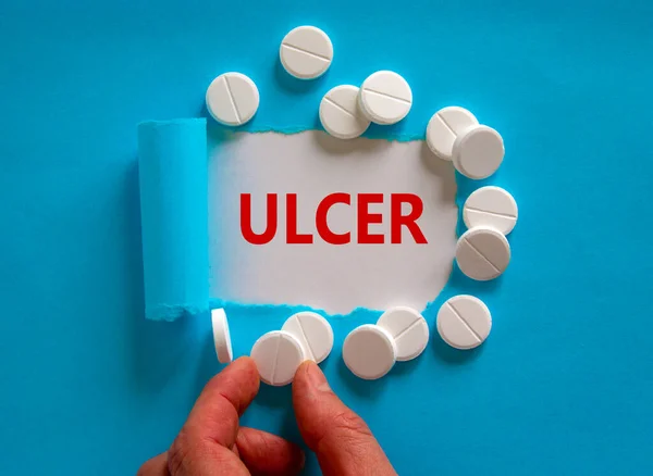 Stomach ulcer symbol. The word 'ulcer' appearing behind torn blue paper, white pills. Doctor hand. Medical and stomach ulcer concept. Copy space.