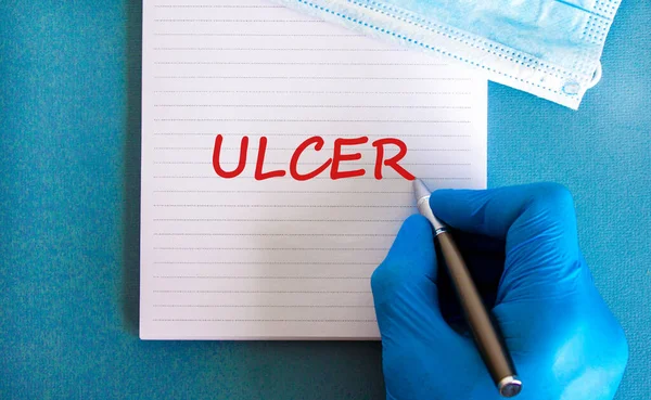 Medical and stomach ulcer symbol. Doctor hand, metalic pen. White note with the word \'ulcer\'. Beautiful blue background. Doctor hand in blue glove. Medical and stomach ulcer concept. Copy space.