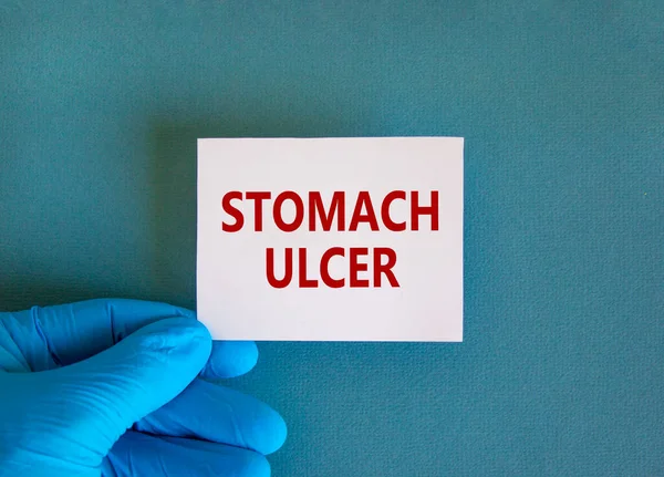 Medical and stomach ulcer symbol. Doctor hand. White card with words \'stomach ulcer\'. Beautiful blue background. Doctor hand in blue glove. Medical and stomach ulcer concept. Copy space.