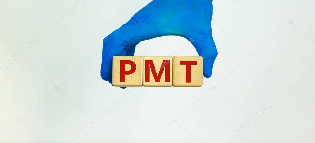 Medical and PMT, premenstrual tension symbol. Hand in blue glove holds wooden cubes with the word 'PMT'. Beautiful white background. Medical and PMT, premenstrual tension concept. Copy space.