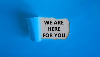 Destek sembolü. 'Senin için buradayız' kelimeleri yırtık mavi kağıdın arkasında beliriyor. Güzel mavi arka plan. İş ve destek kavramı. Boşluğu kopyala.