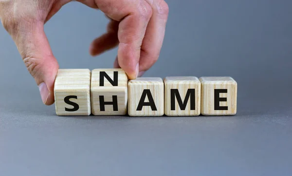 Name or shame symbol. Businessman turns wooden cubes and changes the word \'shame\' to \'name\' or vice versa. Beautiful grey background, copy space. Business, name or shame concept.