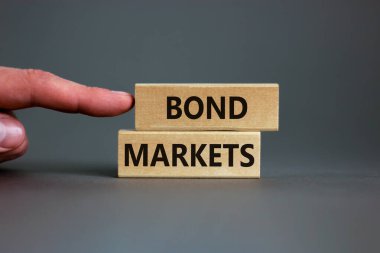 Tahvil piyasası sembolü. Gri arka planda 'Bond piyasaları' yazan tahta bloklar, kopyalama alanı. İşadamı eli. İş ve tahvil piyasaları kavramı.