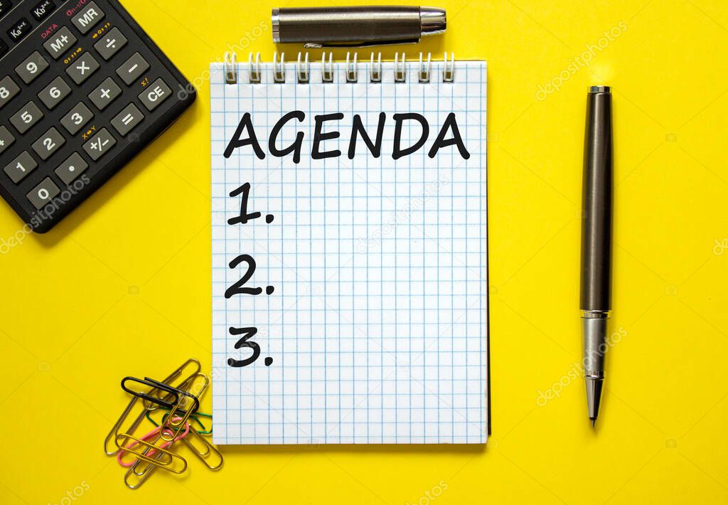 Agenda symbol. White note with the concept word 'agenda' on beautiful yellow table, paper clips, metallic pen and calculator. Business, agenda concept.