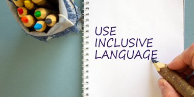 Çeşitlilik, kapsayıcı dil sembolü. İş adamı konsept kelimeler yazıyor, beyaz notada 'kapsayıcı dil', mavi arka planda izole. Çantada bir sürü kalem var. Psikolojik, kapsama konsepti.