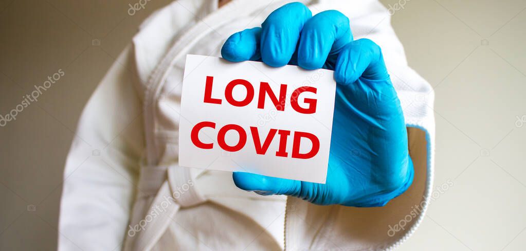 COVID-19 long covid symbol. A young strong man in a white kimono for sambo, jiu jitsu and other martial arts with a blue medical gloves. White card with words 'long covid'. Long covid concept.