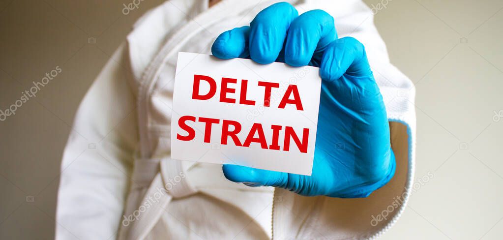 COVID-19 delta indian strain symbol. A young strong man in a white kimono for sambo, jiu jitsu and other martial arts, blue medical gloves. White card with words 'delta strain'. Delta strain concept.