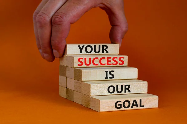 Your success is our goal symbol. Wooden blocks with words \'your success is our goal\'. Businessman hand. Beautiful orange background, copy space. Success business goal concept.