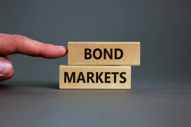 Tahvil piyasası sembolü. Gri arka planda 'Bond piyasaları' yazan tahta bloklar, kopyalama alanı. İşadamı eli. İş ve tahvil piyasaları kavramı.