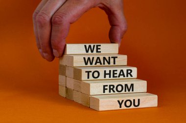 Destek ve yardım sembolü. Tahta bloklar, 'senden duymak istediğimiz' kelimelerle. İşadamı eli. Güzel turuncu arkaplan, kopyalama alanı. İş, yardım ve destek kavramı.