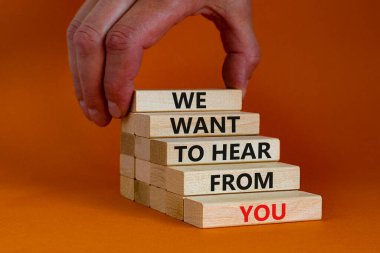 Destek ve yardım sembolü. Tahta bloklar, 'senden duymak istediğimiz' kelimelerle. İşadamı eli. Güzel turuncu arkaplan, kopyalama alanı. İş, yardım ve destek kavramı.