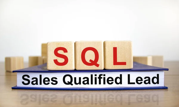 SQL sales qualified lead symbol. Wooden cubes on book with words \'SQL sales qualified lead\'. White background. Business and SQL sales qualified lead concept. Copy space.
