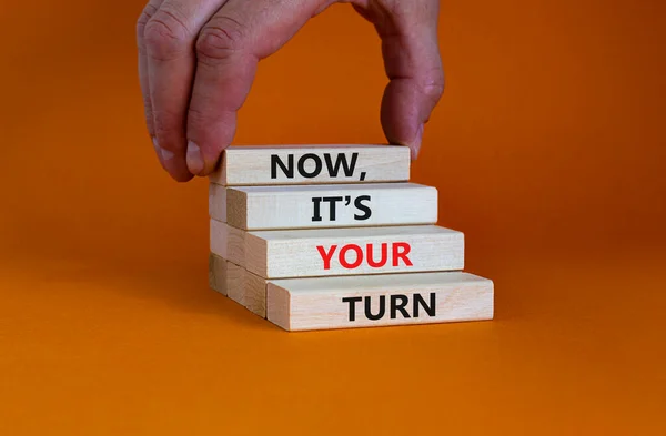 Now, it\'s your turn symbol. Wooden blocks form the words \'now, it\'s your turn\' on beautiful orange background. Businessman hand. Beautiful background. Business, motivational and your turn concept.