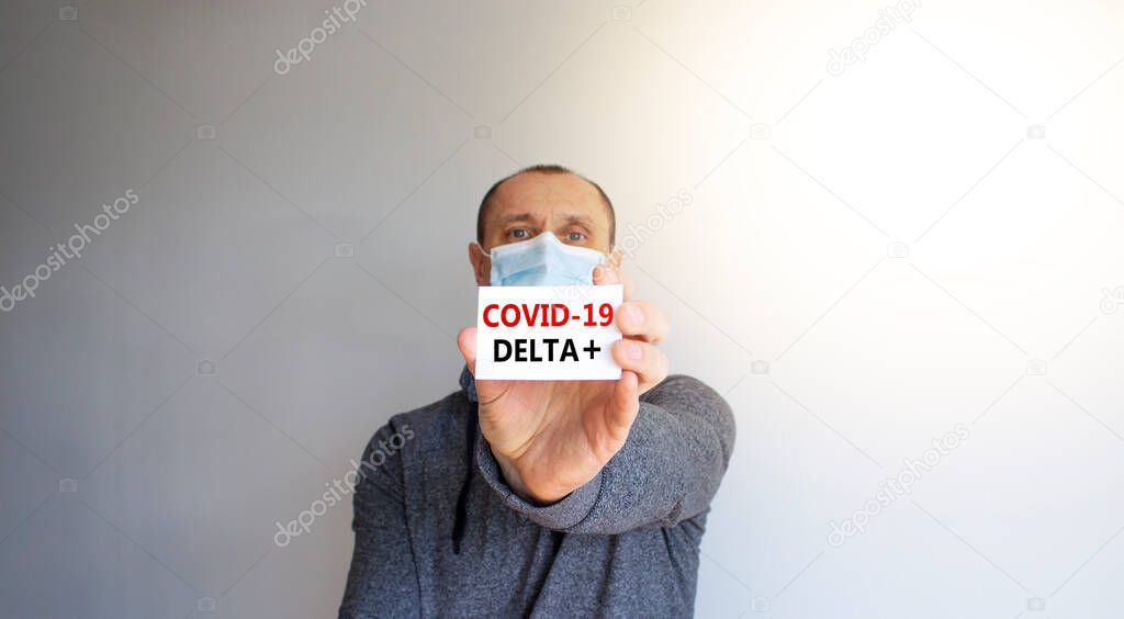 COVID-19 delta plus variant symbol. White card, words Covid-19 delta plus. A young man in a grey wear and medical mask. Sunshine. Beautiful white background. COVID-19 delta plus variant concept.