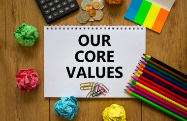 Our core values symbol. White note with words 'Our core values' on beautiful wooden table, colored paper, colored pencils, paper clips, coins and calculator. Business and our core values concept.