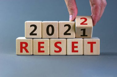 İş planlama konsepti 2022 sıfırlama sembolü. İşadamı ahşap küpü çeviriyor ve '2021' i sıfırla 'yı' 2022 'ye sıfırla' olarak değiştiriyor. Güzel gri arkaplan, kopyalama alanı. İş ve 2022 konsepti sıfırladı.