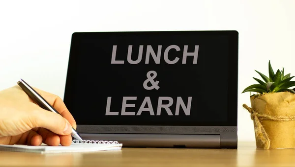Lunch and learn symbol. Tablet with words \'Lunch and learn\'. Businessman hand with pen, house plant. Beautiful white background. Business, educational and lunch and learn concept, copy space.
