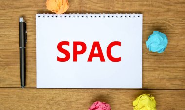SPAC, özel amaçlı şirket sembolü. Sözcükler SPAC, özel amaçlı satın alma şirketi beyaz banknot üzerinde güzel ahşap masa, renkli kağıt, siyah metal kalem. İş ve SPAC kavramı.