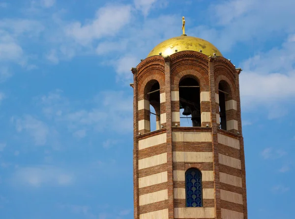 Religion symbol. Beautiful church tower with cross, toller and red tile roof against a bright blue sky with flying birds and fluffy clouds. Religion and nature concept.