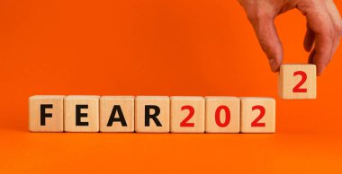 2022 yılbaşı sembolünden korkuyor. İş adamı ahşap bir küp tutuyor, 'Fear 2022' yazıyor. Güzel turuncu arkaplan, kopyalama alanı. İş dünyası, 2022 Yeni yıl konseptinden korkuyor.