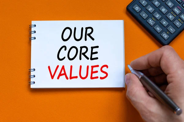 Our core values symbol. Businessman writing words \'Our core values\' on white note. Black calculator. Beautiful orange background. Business and our core values concept. Copy space.