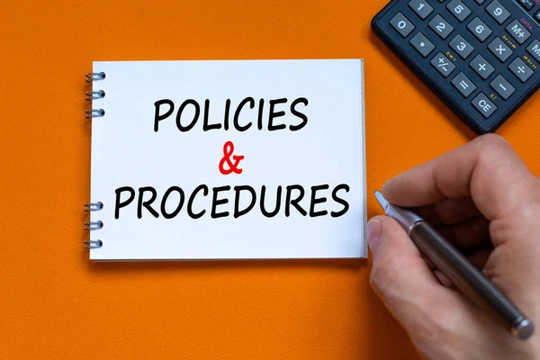 Policies and procedures symbol. Businessman writing words \'Policies and procedures\' on white note. Black calculator. Beautiful orange background. Business, policies and procedures concept. Copy space.