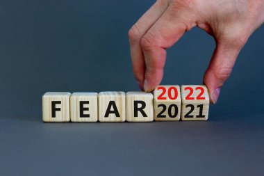 2022 yılbaşı sembolünden korkuyor. İş adamı ahşap küpü değiştirip 'Fear 2021' i 'Fear 2022' olarak değiştiriyor. Güzel gri arkaplan, kopyalama alanı. İş dünyası, 2022 Yeni yıl konseptinden korkuyor.