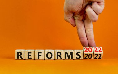 2022 reformları yeni yıl sembolü. İşadamı ahşap küpü değiştiriyor ve '2021 reformları' 2022 reformlarına çeviriyor. Güzel turuncu arkaplan, kopyalama alanı. İş, 2022 Reformlar Yeni Yıl Konsepti.