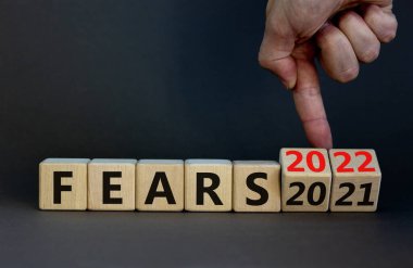 2022 yılbaşı sembolünden korkuyor. İş adamı ahşap küpleri değiştirip '2021 Korkular 2022' olarak değiştiriyor. Güzel gri arkaplan, kopyalama alanı. İş dünyası, 2022 yeni yıl kavramından korkuyor.
