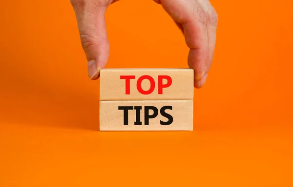 Top tips symbol. Concept words Top tips on wooden blocks on a beautiful orange background. Businessman hand. Business and Top tips concept, copy space.