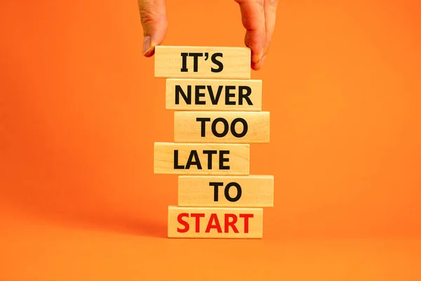 Success start symbol. Wooden blocks with words \'It is never too late to start\'. Businessman hand. Beautiful orange background, copy space. Business and It is never too late to start concept.
