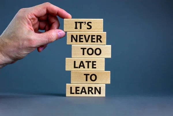 Learn symbol. Wooden blocks with words 'It is never too late to learn'. Businessman hand. Beautiful grey background, copy space. Business and It is never too late to learn concept.
