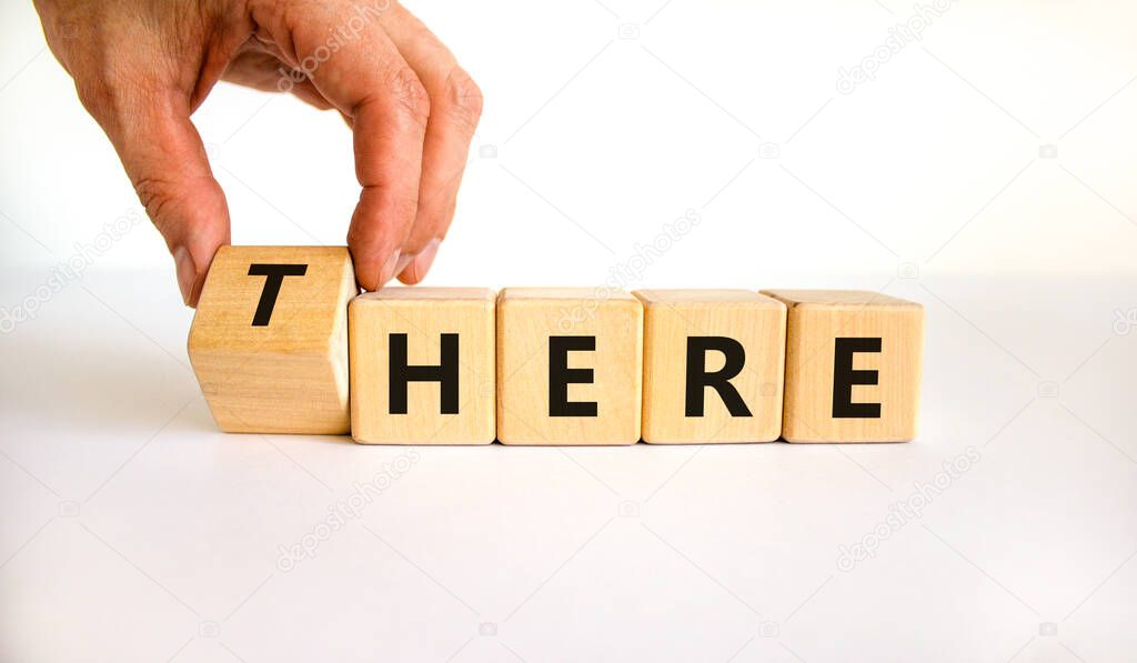 There or here symbol. Businessman turns a wooden cube, changes the word 'there' to 'here'. Beautiful white table, white background, copy space. Business, there or here concept.