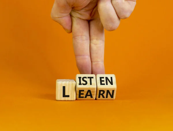Listen and learn symbol. Businessman turns wooden cubes and changes a concept word \'listen\' to \'learn\' on a beautiful orange background. Copy space. Business, educational and listen and learn concept.