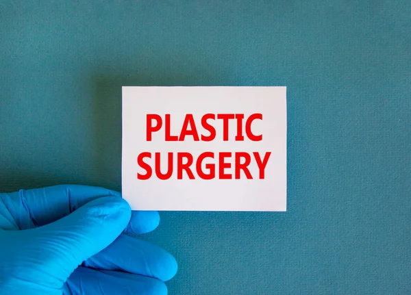 Plastic surgery symbol. White note with words Plastic surgery, beautiful blue background, doctor hand in blue glove. Medical and plastic surgery concept.