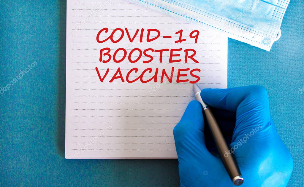 Covid-19 booster shots vaccines symbol. White note with words Covid-19 booster vaccines, beautiful blue background, doctor hand and metallic pen. Medical mask. Covid-19 booster shots vaccines concept.