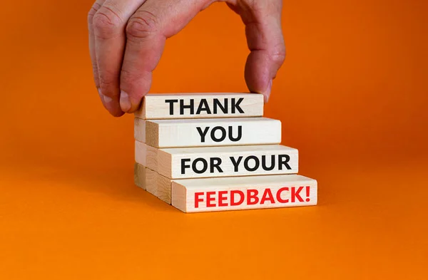Thank you for your feedback symbol. Wooden blocks with concept words \'Thank you for your feedback\'. Businessman hand. Beautiful orange background. Business and your feedback concept. Copy space.