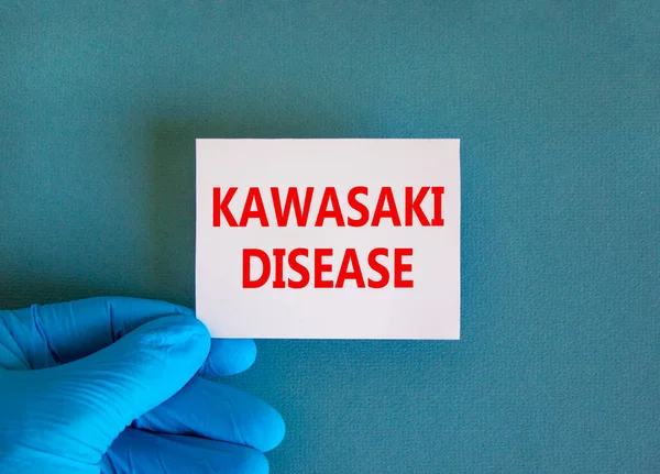 Kawasaki disease symbol. White note with words Kawasaki disease, beautiful blue background, doctor hand in blue glove. Medical and Kawasaki disease concept.
