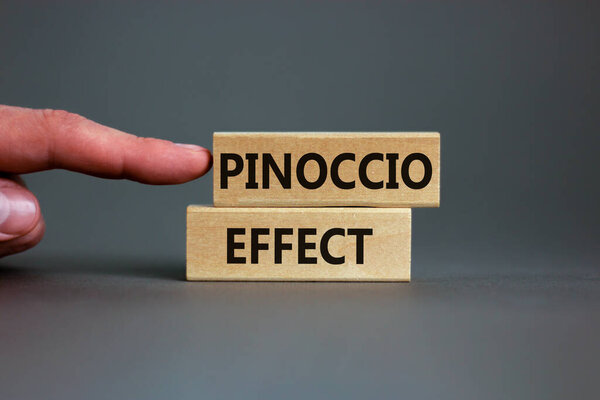 Pinoccio effect symbol. Concept words Pinoccio effect on wooden blocks on a beautiful grey background. Businessman hand. Business and Pinoccio effect concept, copy space.