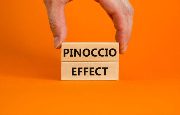 Pinoccio effect symbol. Concept words Pinoccio effect on wooden blocks on a beautiful orange background. Businessman hand. Business and Pinoccio effect concept, copy space.