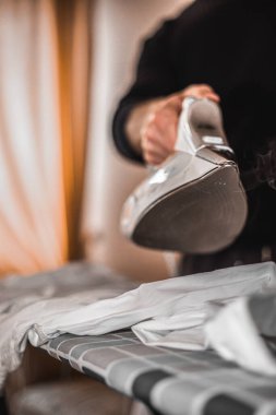 Adam giysileri ütülüyor. Evle ilgilenmek, ev işlerinde erkeklere yardım etmek. Genç adam tişörtünü ütülüyor. Yumuşak odak.