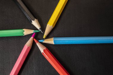 Siyah bir masanın üzerindeki renkli kalemlerin arka planı. Merkez çemberin yarıçapı birliği kavramına yoğunlaşma ve çekim fikri liderlik, topluluk, takım tek bir hedefe odaklandı..