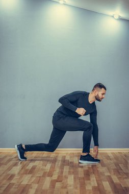Adam dizlerini esnetiyor. Gri arka planda spor yapan adamın fotoğrafı. Spor.