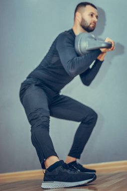 Genç vücut geliştirici kettlebell ile egzersiz yapıyor. Gri arka planda mükemmel fiziği olan kaslı bir erkek. Kuvvet ve motivasyon.