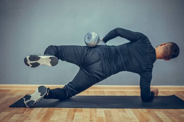 Genç vücut geliştirici kettlebell ile egzersiz yapıyor. Gri arka planda mükemmel fiziği olan kaslı bir erkek. Kuvvet ve motivasyon.