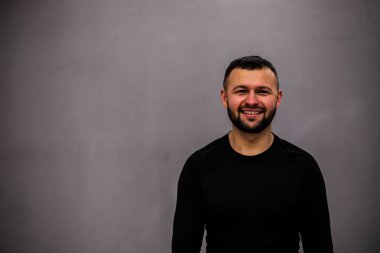 Gri arka planda elleri çapraz olan kendine güvenen sakallı bir adam..