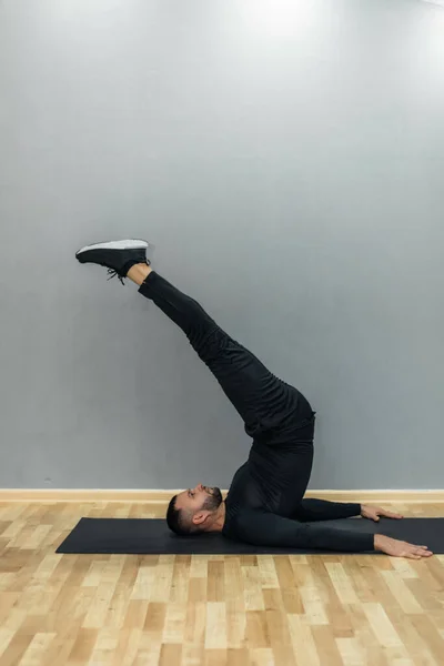 Confident young fitness man exercising on a fitness mat indoors, over gray wall background.